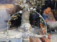 Ein weißer Engel aus der Krippe St. Johannis trägt einen Rosenbogen. Im Hintergrund rechts Maria, Josef und die Krippe.